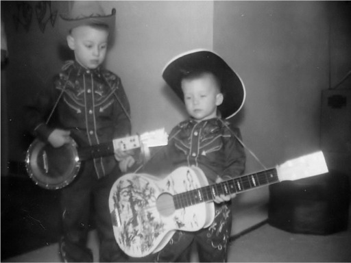 Jim and Will Schubert as children wearing cowboy hats and holding instruments.